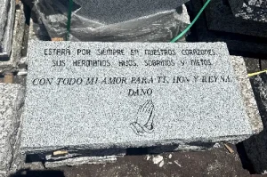 A granite tombstone with Spanish engraving dedicated to a loved one. It features a pair of praying hands and an inscription expressing everlasting love from family members.