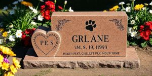 A pet headstone in the shape of a heart sits beside a larger rectangular stone. The larger stone has a paw print design. Colorful flowers surround the gravestone.